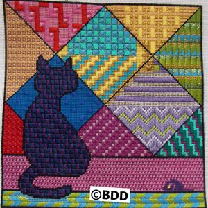 A cat sitting on the ground in front of a colorful quilt.