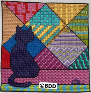 A cat sitting on the ground in front of a colorful quilt.