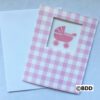 A pink baby carriage card sitting next to an open envelope.