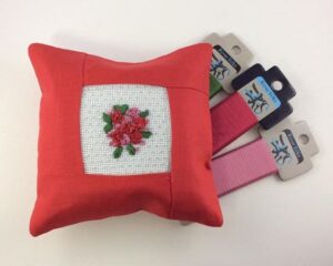 Red pillow with embroidered flowers and floss.