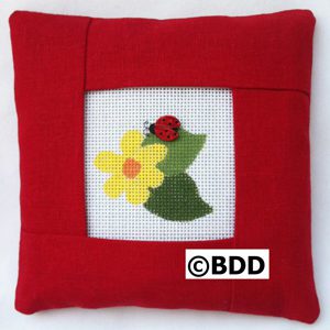 A red pillow with a picture of a ladybug and flower.