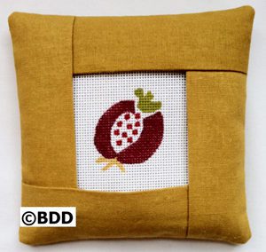 A pillow with an embroidered picture of a pomegranate.