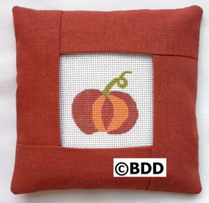 A red pillow with an orange pumpkin on it.