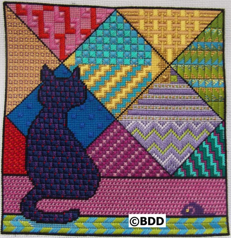 A cat sitting on the ground in front of a colorful quilt.