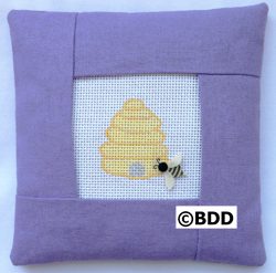 A purple pillow with a bee on it.