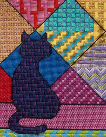 A cat sitting on the ground in front of a quilt.