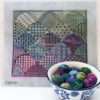 A bowl of yarn and a cross stitch pattern.