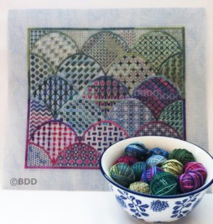 A bowl of yarn and a cross stitch pattern.