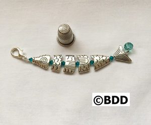 A silver fish charm with green beads on it.