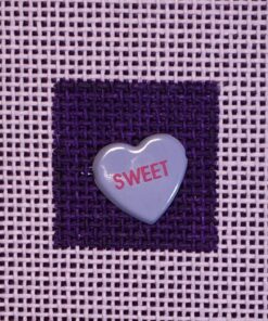 A heart shaped candy is on the purple fabric.