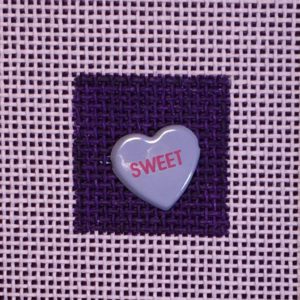 A heart shaped candy is on the purple fabric.