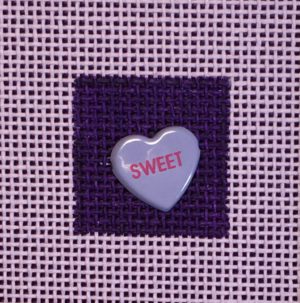 A heart shaped candy is on the purple fabric.