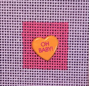 A heart shaped pin with the words " oh baby !" written on it.