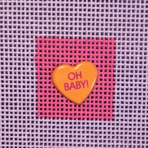 A heart shaped pin with the words " oh baby !" written on it.