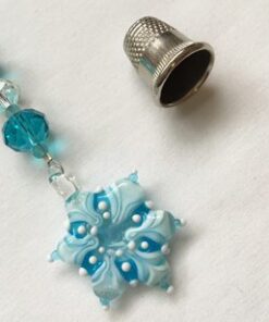 A blue bead and silver thimble on white paper.
