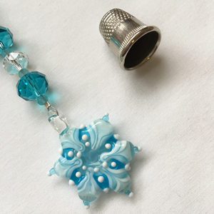 A blue bead and silver thimble on white paper.