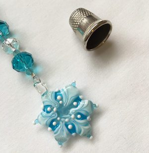 A blue bead and silver thimble on white paper.