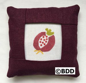 A pillow with an embroidered picture of a pomegranate.