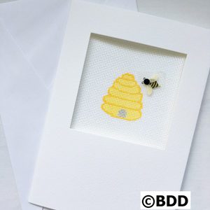 A bee and beehive picture in a white frame.