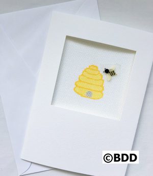 A bee and beehive picture in a white frame.