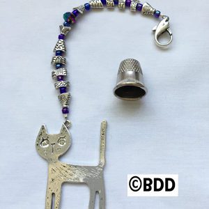 A cat charm with a thimble and bead attached to it.