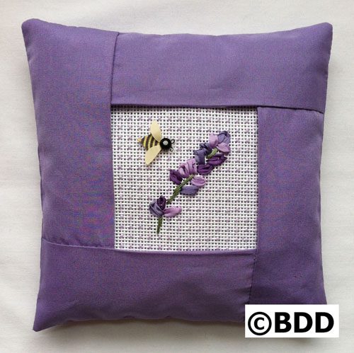 A purple pillow with a bee and flowers on it.