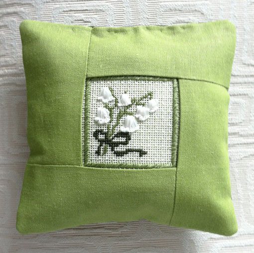 A green pillow with a cross stitch design on it.