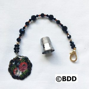 A black beaded keychain with a thimble and a rose charm.