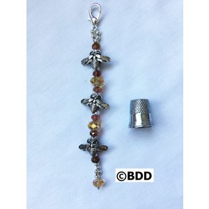 A silver charm with beads and a thimble