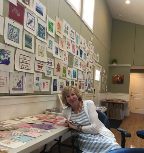 A woman sitting at a table with many cards on the wall.