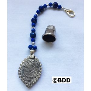 A silver pendant with blue beads and a thimble.