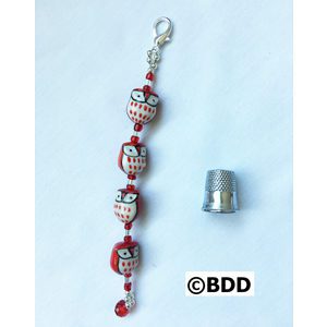 A red and white skull bead bracelet with a thimble.