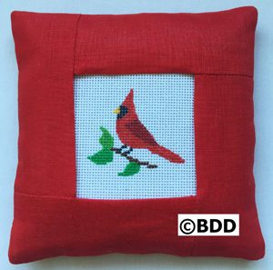 A red pillow with a picture of a cardinal on it.