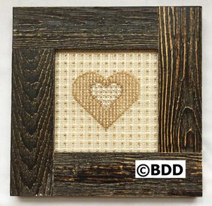 A cross stitch heart in a wooden frame.