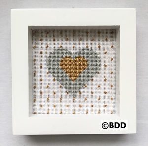 A framed picture of a heart with gold and silver thread.