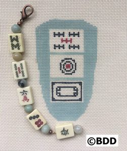 A cross stitch of a mahjong tile and beads.