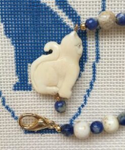 A cat is sitting on the chain of a beaded necklace.
