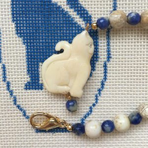 A cat is sitting on the chain of a beaded necklace.