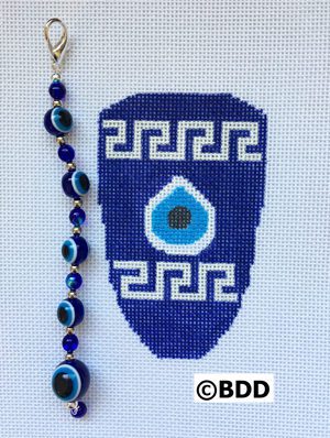 A blue and white cross stitch ornament with an evil eye bead.