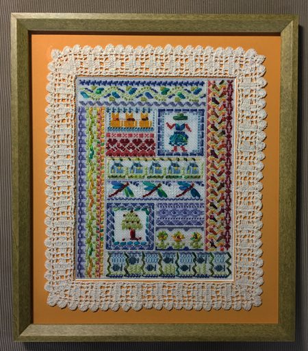 A framed picture of a quilt with lace trim.