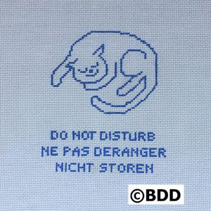 A cross stitch pattern of a cat with the caption " do not disturb ne pas deranger nicht storen ".