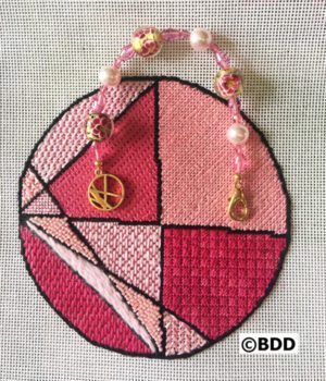 A pink cross stitch ornament with peace sign.