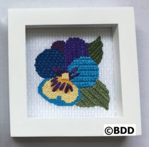 A cross stitch picture of a pansy flower.