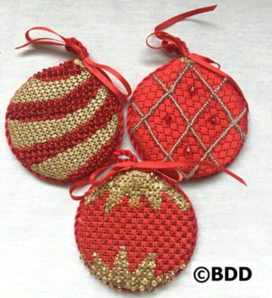 Three red and gold ornaments are sitting on a table.