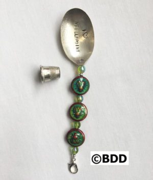 A spoon with a green bead and a silver handle.