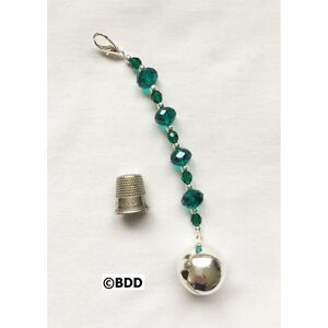 A green bead and bell hanging from the side of a string.