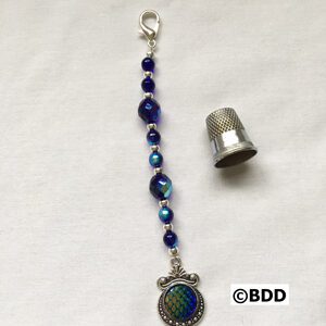 A silver thimble and blue beads with a peacock charm.