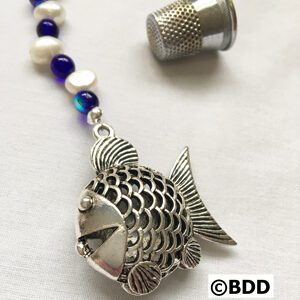 A fish shaped silver locket with blue beads.