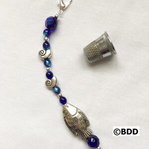 A blue bead and silver fish charm on a white background.