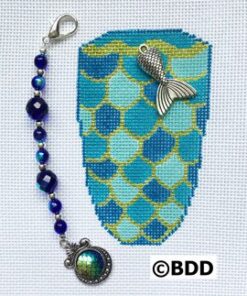 A blue and green cross stitch pattern with a fish charm.